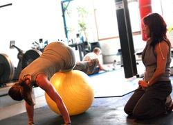 Normal_personal_trainer_monitoring_a_client_s_movement_during_a_fitball_exercise